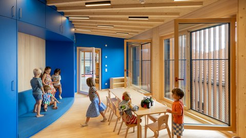 Kinder spielen und sitzen in einem hellen Raum mit blauen Wänden und großen Fenstern