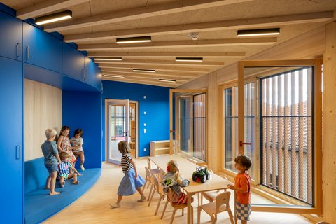 Kinder spielen und sitzen in einem hellen Raum mit blauen Wänden und großen Fenstern