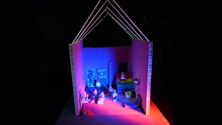 Modell eines offenen Gebäudes mit Figuren, Treppe und farbiger Beleuchtung.