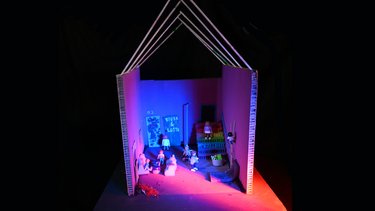 Modell eines offenen Gebäudes mit Figuren, Treppe und farbiger Beleuchtung.