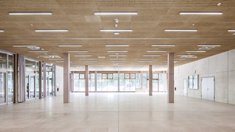 Großer heller Raum mit Holzdecke, vielen Deckenleuchten, großen Fenstern und gläsernen Trennwänden