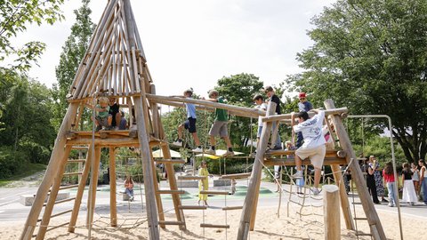 Kinder spielen auf einem Holz-Klettergerüst mit Sandboden in einem Park