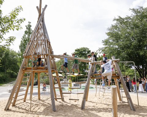 Kinder spielen auf einem Holz-Klettergerüst mit Sandboden in einem Park