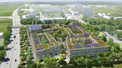 "Luftaufnahme einer modernen Wohnsiedlung in ländlicher Umgebung. Im Vordergrund mehrere vier- bis fünfgeschossige Wohngebäude mit begrünten Dächern, Solarpanelen und integrierten Grünflächen. Die Gebäude sind in Holz- und hellen Steinoptik gestaltet. Ein Spielplatz mit rotem Spielgerät ist zwischen den Gebäuden sichtbar. Dahinter erstrecken sich grüne Wiesen und Bäume. Im Hintergrund große Industriehallen und Gewerbegebäude mit weißen Fassaden. Links eine Hauptstraße mit Fahrzeugen und Straßenbäumen. Die Umgebung ist geprägt von grünen Feldern und vereinzelten Baumgruppen unter bewölktem Himmel."