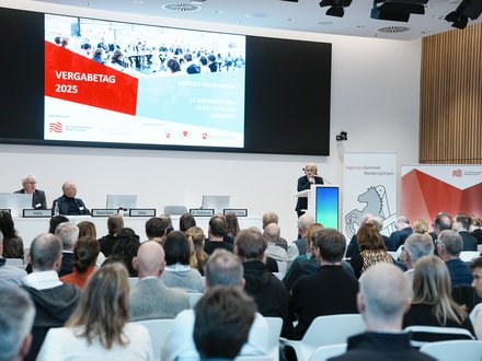Blick in einen voll besetzten Veranstaltungssaal mit Podium, Rednerpult und großer Präsentationsleinwand.