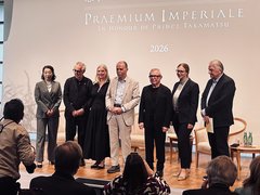 Sieben Personen stehen nebeneinander auf einer Bühne vor einer Leinwand mit der Aufschrift 'PRAEMIUM IMPERIALE IN HONOUR OF PRINCE TAKAMATSU 2026', Publikum im Vordergrund.