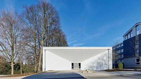 Modernes weißes Gebäude mit markantem Vordach an einer Straße.