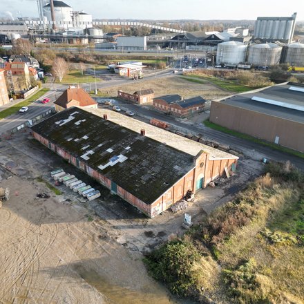 Luftaufnahme eines ehemaligen Industrieareals mit langem Backsteingebäude und angrenzenden Straßen.