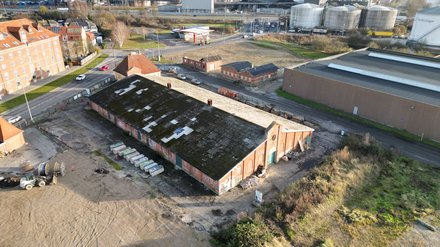 Luftaufnahme eines ehemaligen Industrieareals mit langem Backsteingebäude und angrenzenden Straßen.