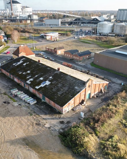 Luftaufnahme eines ehemaligen Industrieareals mit langem Backsteingebäude und angrenzenden Straßen.