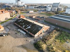 Luftaufnahme eines ehemaligen Industrieareals mit langem Backsteingebäude und angrenzenden Straßen.