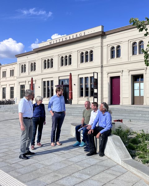Mehrere Personen stehen und sitzen vor dem historischen Bahnhofsgebäude in Wittenberge auf einem neu gestalteten Vorplatz.