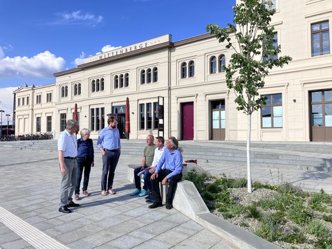 Mehrere Personen stehen und sitzen vor dem historischen Bahnhofsgebäude in Wittenberge auf einem neu gestalteten Vorplatz.
