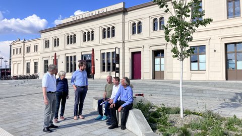 Mehrere Personen stehen und sitzen vor dem historischen Bahnhofsgebäude in Wittenberge auf einem neu gestalteten Vorplatz.