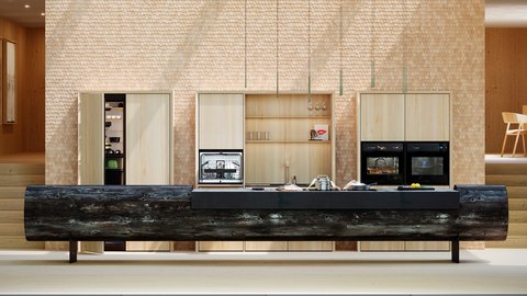 „Eine moderne Designerküche mit einer monumentalen Kücheninsel aus einem Baumstamm vor einer Schindelwand mit integrierten Einbaugeräten.“
