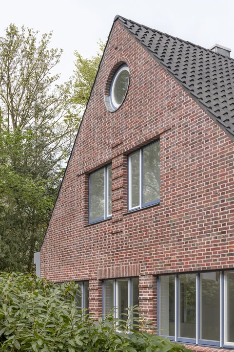 Giebelfassade eines Backsteinhauses mit Satteldach und großen Fenstern.