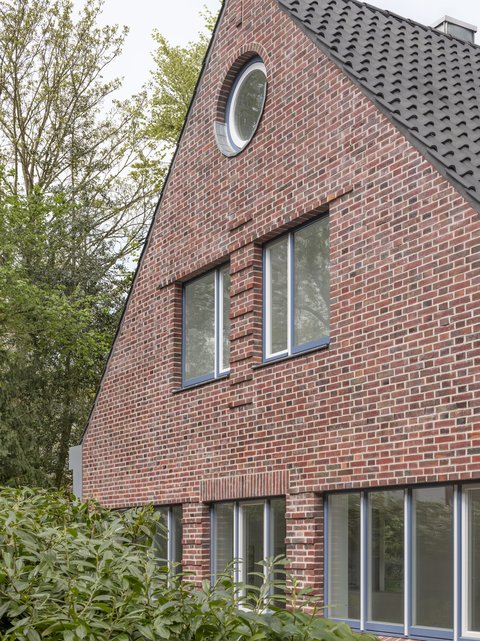 Giebelfassade eines Backsteinhauses mit Satteldach und großen Fenstern.