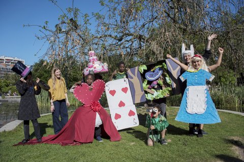 Gruppe von Menschen in fantasievollen Kostümen aus Alice-im-Wunderland-Motiven auf einer Wiese vor Bäumen