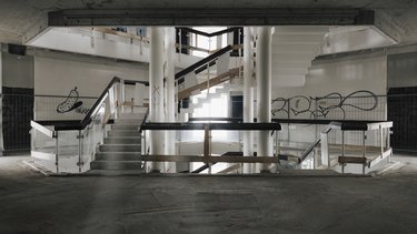 Zentrales Treppenhaus im Rohbau, mehrgeschossiger Luftraum mit Treppen, Geländern und sichtbaren Betonbauteilen.