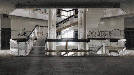 Zentrales Treppenhaus im Rohbau, mehrgeschossiger Luftraum mit Treppen, Geländern und sichtbaren Betonbauteilen.