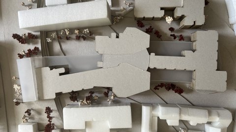 „Draufsicht auf ein städtebauliches Architekturmodell mit weißen Baukörpern und Miniaturbäumen entlang der Straßen und Plätze.“