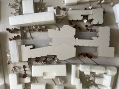 „Draufsicht auf ein städtebauliches Architekturmodell mit weißen Baukörpern und Miniaturbäumen entlang der Straßen und Plätze.“