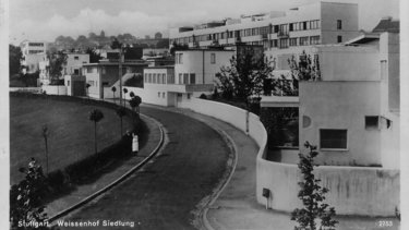 Historische Schwarzweißaufnahme der Weißenhofsiedlung in Stuttgart mit modernen Wohnhäusern entlang einer geschwungenen Straße.