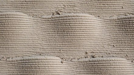 Detailaufnahme der geschichteten Oberfläche einer 3D-gedruckten Lehmwand mit sichtbaren horizontalen Druckschichten und natürlicher Materialtextur.