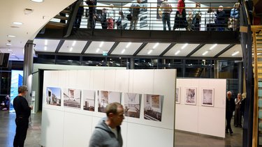 Ausstellungssaal mit Fotowänden, mehreren Besucher:innen und einer Galerieebene.