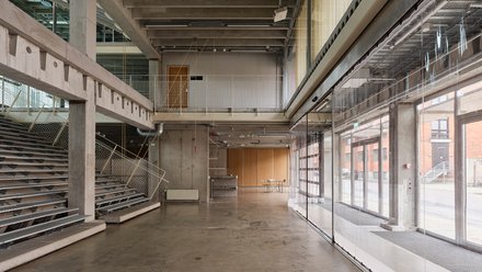 Heller mehrstöckiger Innenraum mit Tribüne auf der linken Seite und einer Fensterfront auf der rechten Seite.