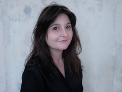 Porträt von Flavia-Ioana Biianu, einer Frau mit dunklen Haaren vor einer hellen Wand.