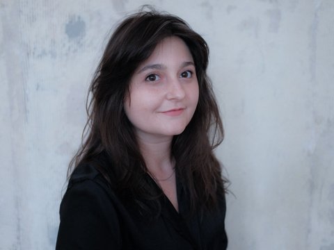 Porträt von Flavia-Ioana Biianu, einer Frau mit dunklen Haaren vor einer hellen Wand.
