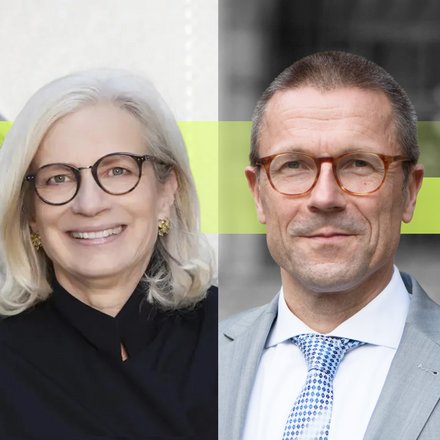 Zwei Personen in formeller Kleidung stehen nebeneinander vor einer modernen Gebäudefassade