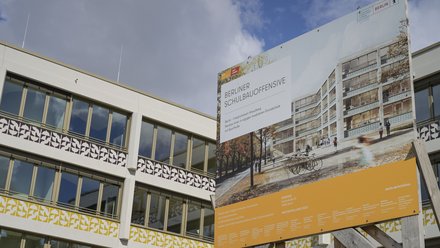 Bauschild der Berliner Schulbauoffensive vor einem modernen Schulgebäude.