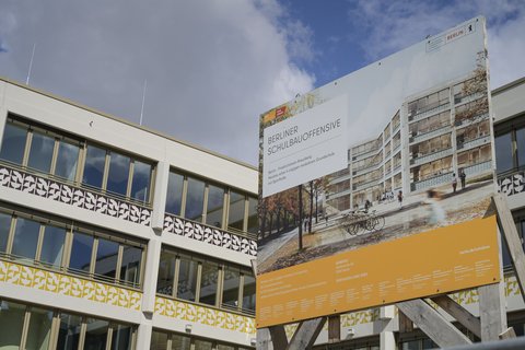 Bauschild der Berliner Schulbauoffensive vor einem modernen Schulgebäude.