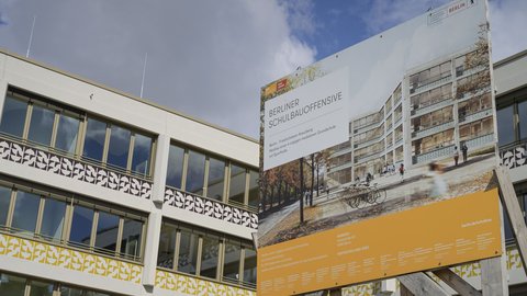 Bauschild der Berliner Schulbauoffensive vor einem modernen Schulgebäude.