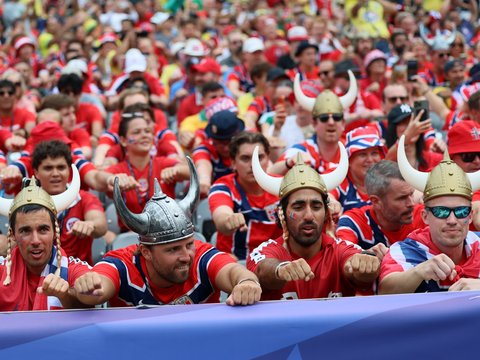 Menschenmenge in roten Fantrikots mit Wikingerhelmen feuert gemeinsam bei einem Public Viewing ihre Mannschaft an.