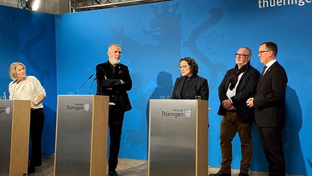 Fünf Personen stehen an Rednerpulten mit dem Schriftzug 'Freistaat Thüringen' vor einer blauen Wand mit Wappen und Schriftzug 'thueringen'.