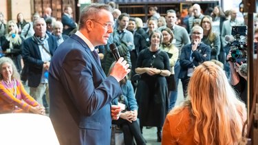 Ansprache: Redner mit Mikrofon spricht vor stehendem Publikum bei einem Event.