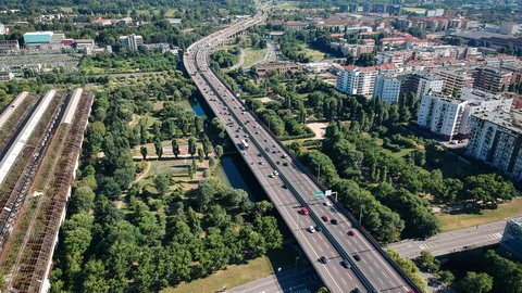 Luftaufnahme einer mehrspurigen Stadtautobahn mit angrenzenden Grünflächen und Wohngebieten.