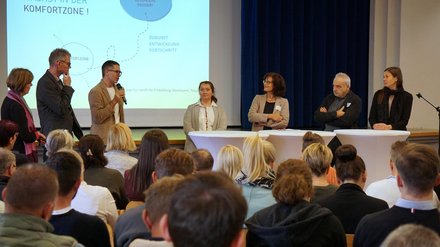 Eine Podiumssituation zeigt mehrere Personen hinter Stehtischen vor einem sitzenden Publikum, im Hintergrund ist eine Präsentationsfläche mit grafischen Inhalten sichtbar, wodurch das Bild eine moderierte Diskussion oder Fachveranstaltung dokumentiert und für Austausch, Meinungsvielfalt und öffentliche Debatte zu gesellschaftlichen oder planerischen Themen steht.