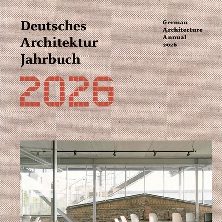 Buchcover „Deutsches Architektur Jahrbuch 2026“ (German Architecture Annual 2026): rosé Strukturhintergrund, unten ein helles Foto eines Industrie‑Innenraums mit Glaswänden, sichtbarer Außentreppe und lose gestellten Stühlen; Logo „DAM Preis 2026“ links unten.