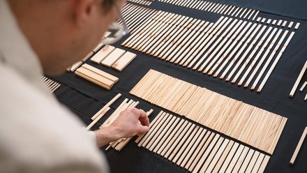 Person sortiert schmale Holzleisten nach Länge auf schwarzem Tisch; geordnete Reihen und Gruppen.