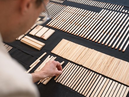Person sortiert schmale Holzleisten nach Länge auf schwarzem Tisch; geordnete Reihen und Gruppen.