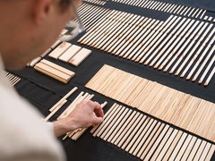 Person sortiert schmale Holzleisten nach Länge auf schwarzem Tisch; geordnete Reihen und Gruppen.
