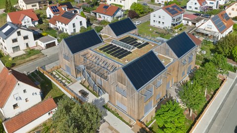 Luftbild: Mehrteiliger Kita‑Komplex in Holzbauweise mit großen Photovoltaikflächen und begrünten Dachbereichen um einen Innenhof.