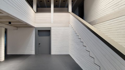 Foyer: Helles Treppenhaus mit weißem Ziegelmauerwerk, breiter Treppenbrüstung, Galerie im Obergeschoss, grauer Tür und dunklem Boden.