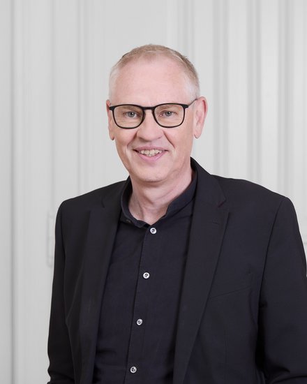 Mann mit Brille vor hellem Hintergrund.