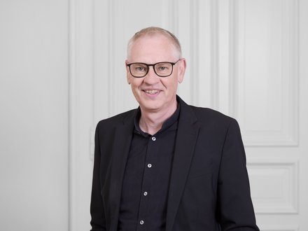 Mann mit Brille vor hellem Hintergrund.