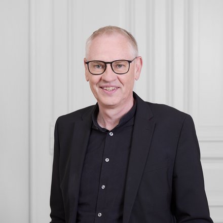 Mann mit Brille vor hellem Hintergrund.